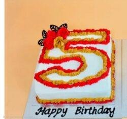Egg-free number 5 birthday cake decorated with red and gold cream piping, floral decorations and chocolate accents.
