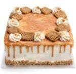 Square fresh cream caramel cake with a rich caramel drip, caramel glaze, fresh cream swirls, and biscuit pieces on top.