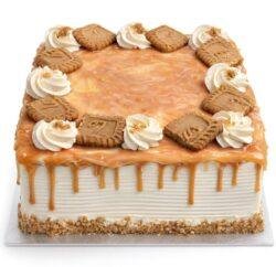 Square fresh cream caramel cake with a rich caramel drip, caramel glaze, fresh cream swirls, and biscuit pieces on top.