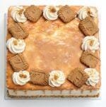 Top view of a square caramel fresh cream cake decorated with caramel glaze, fresh cream swirls, and crunchy biscuit pieces.
