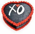 Top view of a heart-shaped black fresh cream cake with red borders and a personalised XO design.