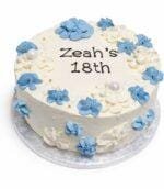Top view of a tall fresh cream birthday cake featuring blue and white floral decorations, pearl accents, and a personalised birthday message.