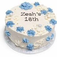 Top view of a tall fresh cream birthday cake featuring blue and white floral decorations, pearl accents, and a personalised birthday message.